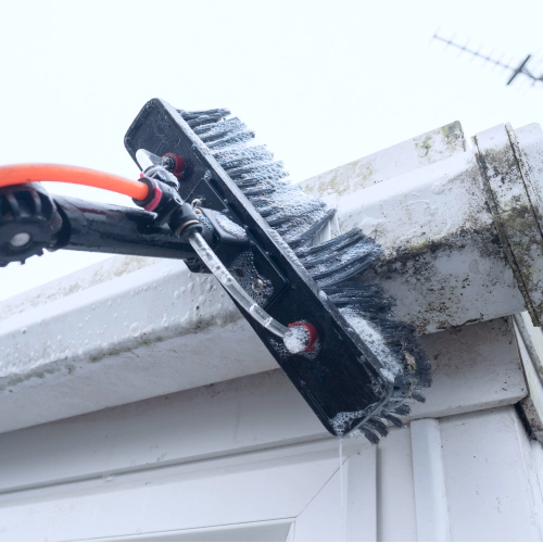 A brush cleaning dirty clogged white plastic pvc gutters and drain pipes with mossy green mould plastic fascias Westminster MA